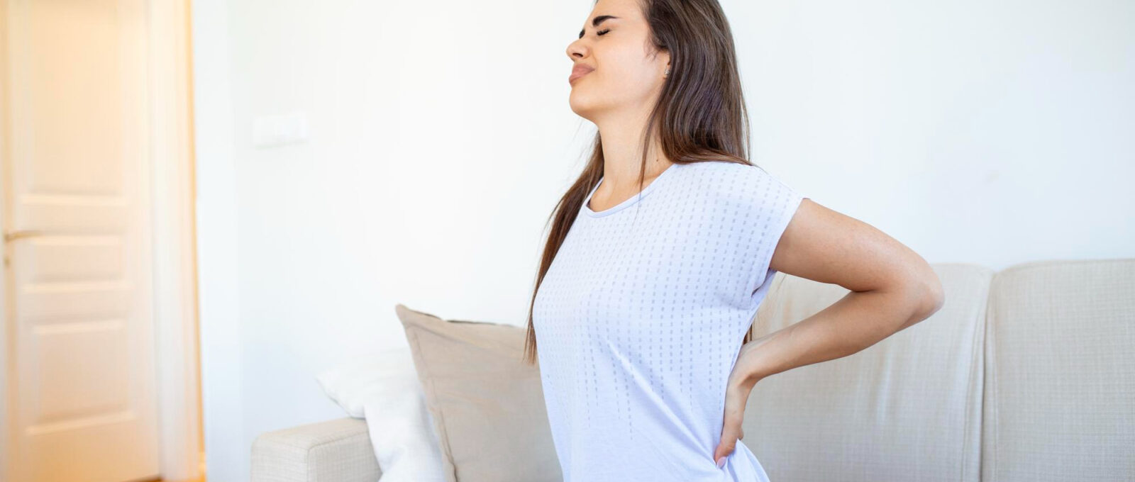 Woman suffering from backache at home Lower Back Pain Woman feels back pain massaging aching muscles sad woman suffers from lowback