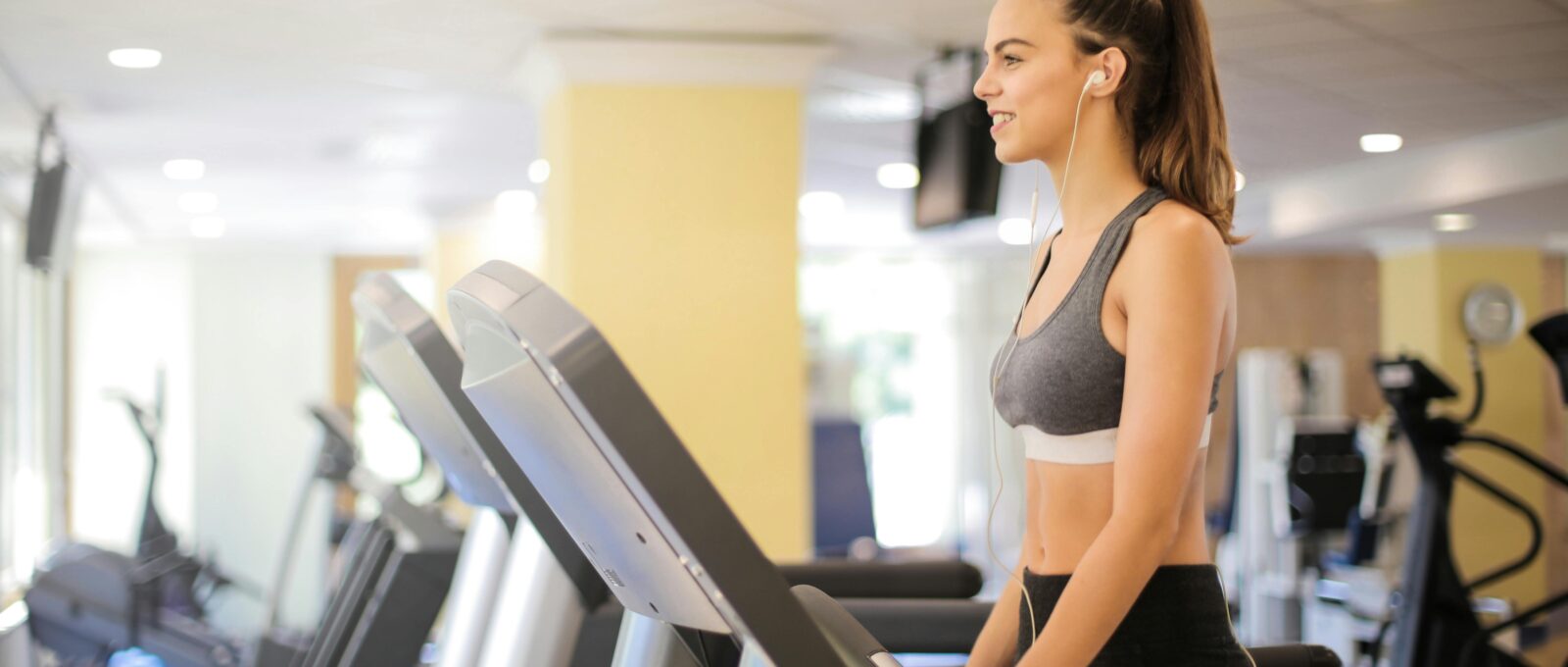 women wearing white earphones is walking on the treadmill in the gym and smiling